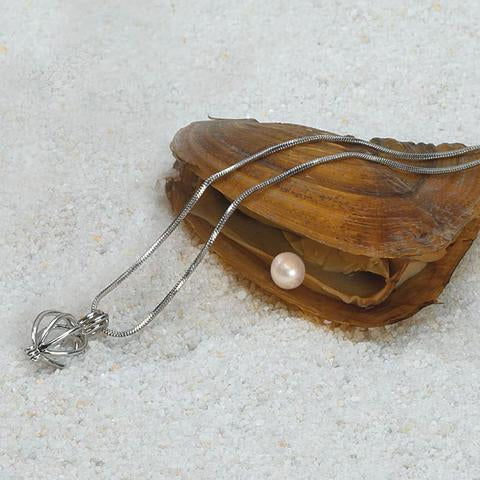 Silver necklace with a pearl pendant on a wooden shell on sandy surface